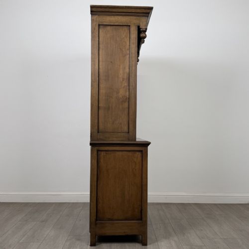 fig 7. A tall antique brown oak cupboard with carved spindle panels on the upper cabinet doors, brass butterfly hinges, two drawers, and a lower open alcove with a blue painted interior.