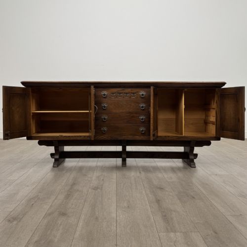 fig 1. A large dark oak sideboard featuring carved panel doors, central drawers, decorative metal hinges, and a stretcher base.
