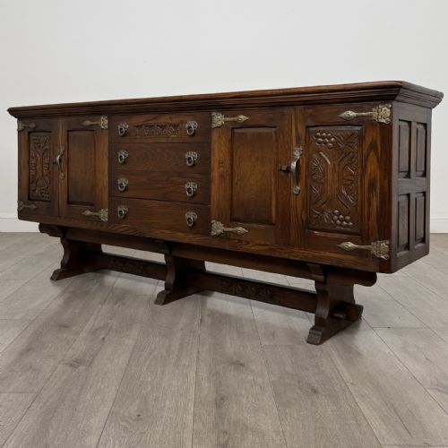 fig 2. A large dark oak sideboard featuring carved panel doors, central drawers, decorative metal hinges, and a stretcher base.
