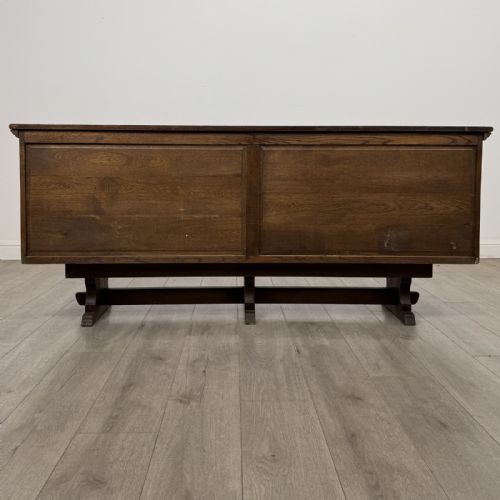 fig 5. A large dark oak sideboard featuring carved panel doors, central drawers, decorative metal hinges, and a stretcher base.