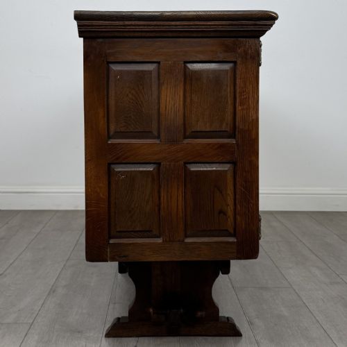 fig 7. A large dark oak sideboard featuring carved panel doors, central drawers, decorative metal hinges, and a stretcher base.