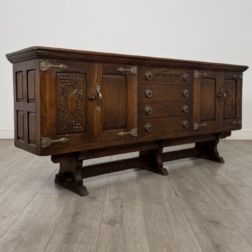 fig 8. A large dark oak sideboard featuring carved panel doors, central drawers, decorative metal hinges, and a stretcher base.