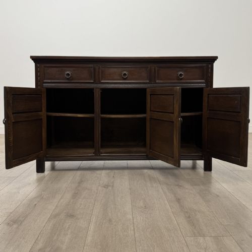 fig 1. A dark oak sideboard featuring three top drawers with metal ring pulls above three carved panel cupboard doors.