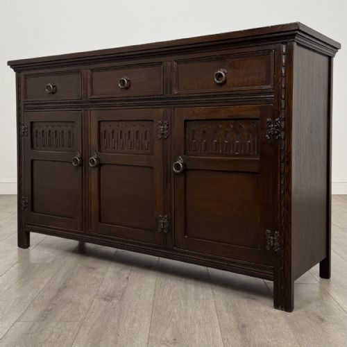 fig 2. A dark oak sideboard featuring three top drawers with metal ring pulls above three carved panel cupboard doors.