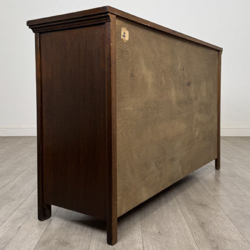 fig 4. A dark oak sideboard featuring three top drawers with metal ring pulls above three carved panel cupboard doors.