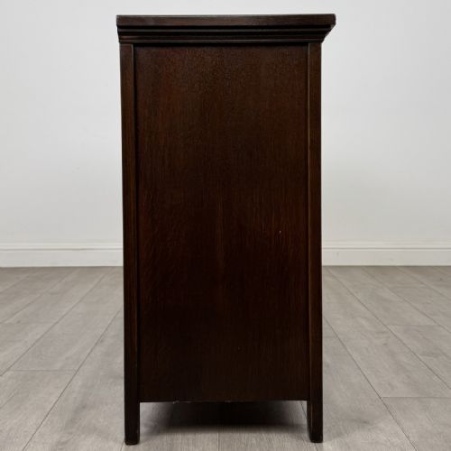 fig 7. A dark oak sideboard featuring three top drawers with metal ring pulls above three carved panel cupboard doors.