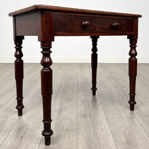 fig 7. A Victorian mahogany writing table featuring a rectangular top, a single drawer with two wooden knobs, and four turned legs.
