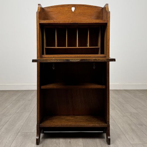 fig 1. An Arts and Crafts golden oak bureau with a heart cutout on the top gallery back, a fall-front writing surface with drop handles, and two open bookshelves underneath.