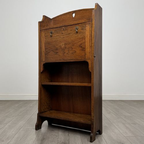 fig 2. An Arts and Crafts golden oak bureau with a heart cutout on the top gallery back, a fall-front writing surface with drop handles, and two open bookshelves underneath.