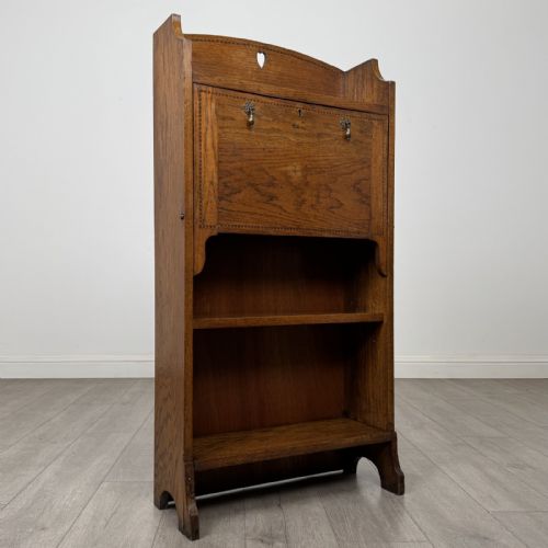 fig 8. An Arts and Crafts golden oak bureau with a heart cutout on the top gallery back, a fall-front writing surface with drop handles, and two open bookshelves underneath.