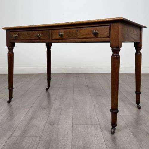 fig 1. An antique golden oak writing table featuring two frieze drawers with turned knobs and supported by turned legs on brass castors.