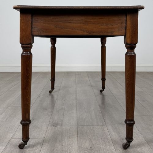 fig 2. An antique golden oak writing table featuring two frieze drawers with turned knobs and supported by turned legs on brass castors.