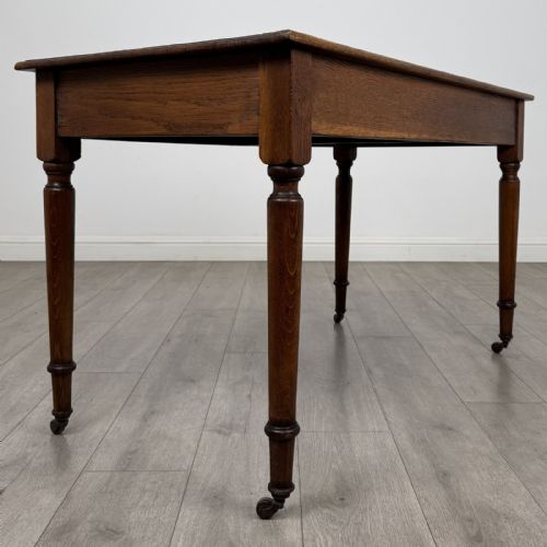 fig 3. An antique golden oak writing table featuring two frieze drawers with turned knobs and supported by turned legs on brass castors.