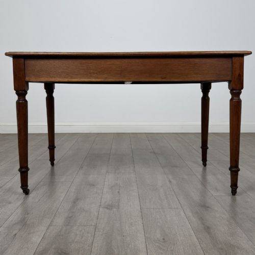 fig 4. An antique golden oak writing table featuring two frieze drawers with turned knobs and supported by turned legs on brass castors.