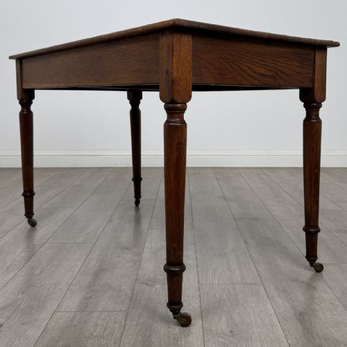 fig 5. An antique golden oak writing table featuring two frieze drawers with turned knobs and supported by turned legs on brass castors.
