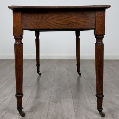 fig 6. An antique golden oak writing table featuring two frieze drawers with turned knobs and supported by turned legs on brass castors.