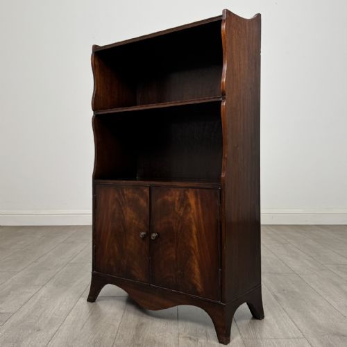 fig 3. An antique mahogany open bookcase featuring a shaped raised gallery top, two upper shelf spaces, and a lower two-door cabinet with flame mahogany veneered panels.