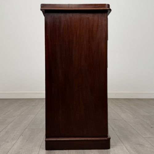 fig 5. A Victorian mahogany chest of drawers featuring a two-over-three drawer configuration, brass cup handles, and a plinth base.
