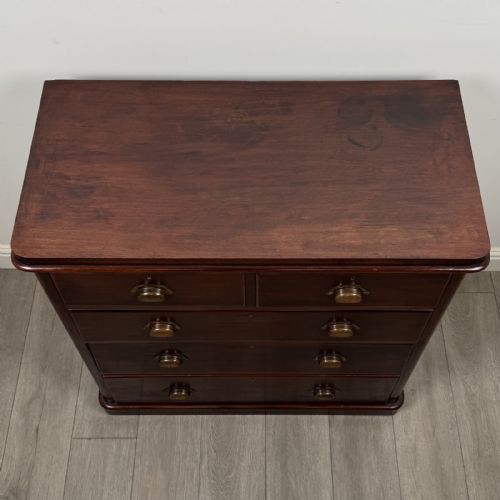 fig 7. A Victorian mahogany chest of drawers featuring a two-over-three drawer configuration, brass cup handles, and a plinth base.
