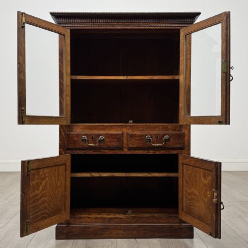 fig 1. A dark oak Victorian display cabinet featuring a dentil cornice, glazed upper doors, two drawers with brass handles, and panelled lower cupboard doors.