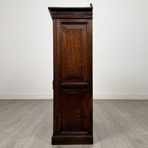 fig 3. A dark oak Victorian display cabinet featuring a dentil cornice, glazed upper doors, two drawers with brass handles, and panelled lower cupboard doors.
