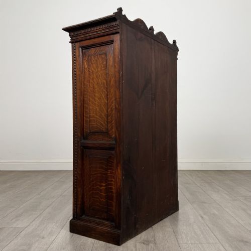 fig 4. A dark oak Victorian display cabinet featuring a dentil cornice, glazed upper doors, two drawers with brass handles, and panelled lower cupboard doors.