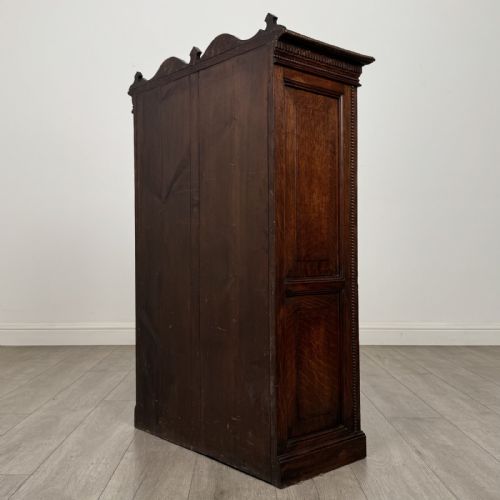 fig 6. A dark oak Victorian display cabinet featuring a dentil cornice, glazed upper doors, two drawers with brass handles, and panelled lower cupboard doors.