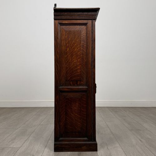 fig 7. A dark oak Victorian display cabinet featuring a dentil cornice, glazed upper doors, two drawers with brass handles, and panelled lower cupboard doors.