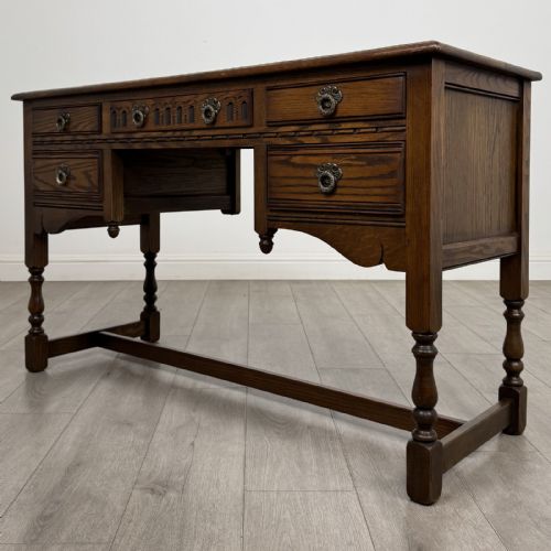 fig 1. An antique dark oak writing desk featuring five carved drawers with metal drop handles, turned legs, and lower stretchers.