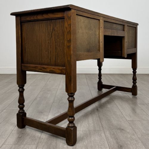 fig 3. An antique dark oak writing desk featuring five carved drawers with metal drop handles, turned legs, and lower stretchers.