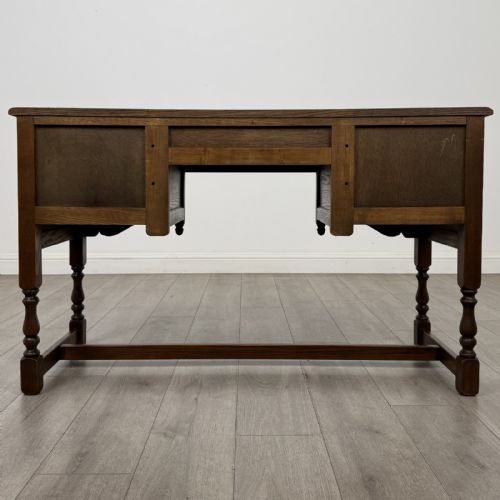 fig 4. An antique dark oak writing desk featuring five carved drawers with metal drop handles, turned legs, and lower stretchers.