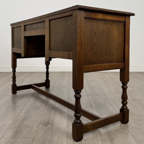 fig 5. An antique dark oak writing desk featuring five carved drawers with metal drop handles, turned legs, and lower stretchers.