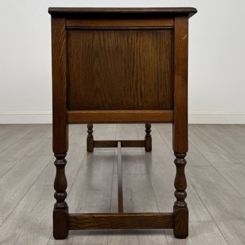fig 6. An antique dark oak writing desk featuring five carved drawers with metal drop handles, turned legs, and lower stretchers.