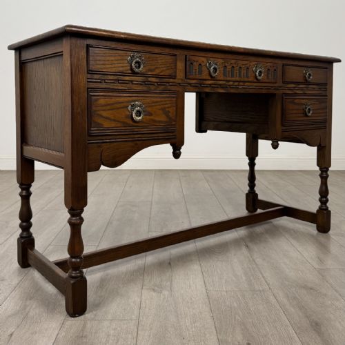 fig 7. An antique dark oak writing desk featuring five carved drawers with metal drop handles, turned legs, and lower stretchers.