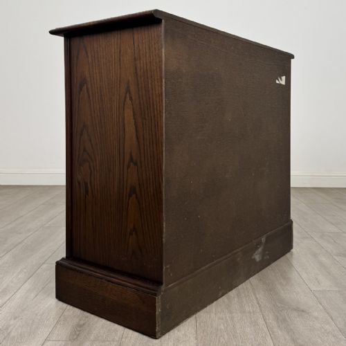 fig 1. A dark brown oak storage cupboard featuring two top drawers above twin doors with carved linenfold panels and brass handles.