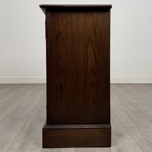 fig 3. A dark brown oak storage cupboard featuring two top drawers above twin doors with carved linenfold panels and brass handles.