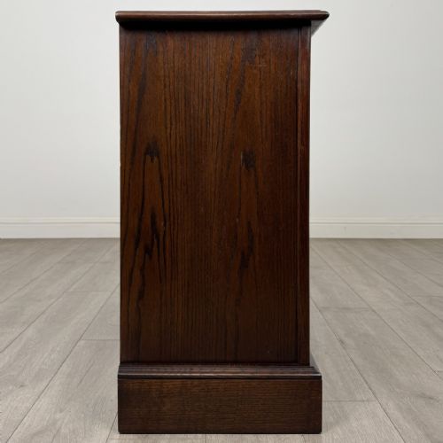 fig 5. A dark brown oak storage cupboard featuring two top drawers above twin doors with carved linenfold panels and brass handles.