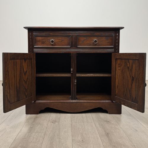 fig 6. A dark brown oak storage cupboard featuring two top drawers above twin doors with carved linenfold panels and brass handles.