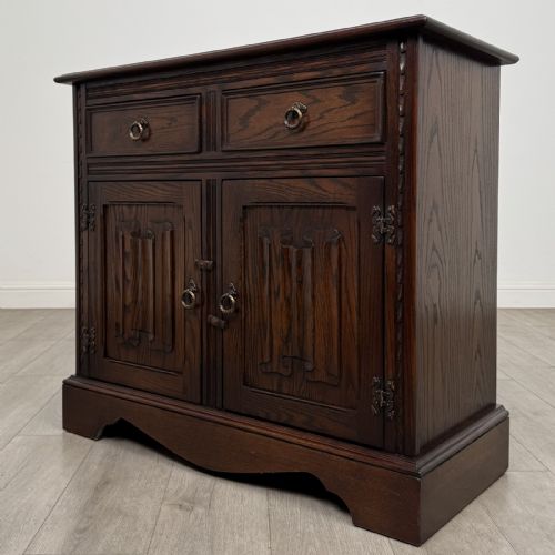 fig 7. A dark brown oak storage cupboard featuring two top drawers above twin doors with carved linenfold panels and brass handles.