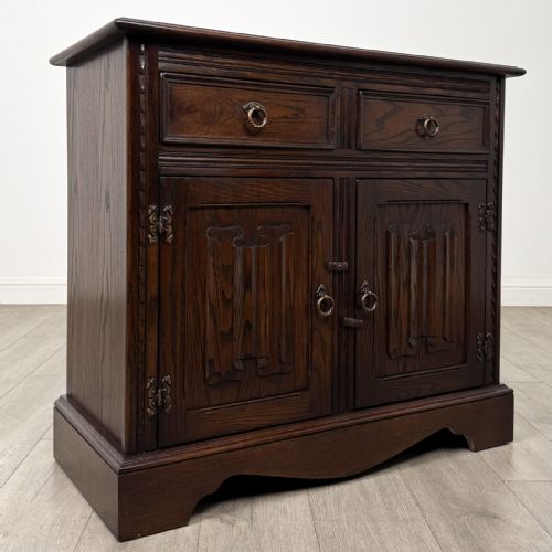 fig 8. A dark brown oak storage cupboard featuring two top drawers above twin doors with carved linenfold panels and brass handles.
