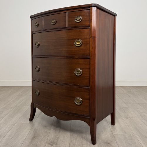 fig 1. An antique mahogany chest of drawers with a bowfront shape, brass oval handles, and reeded side columns.