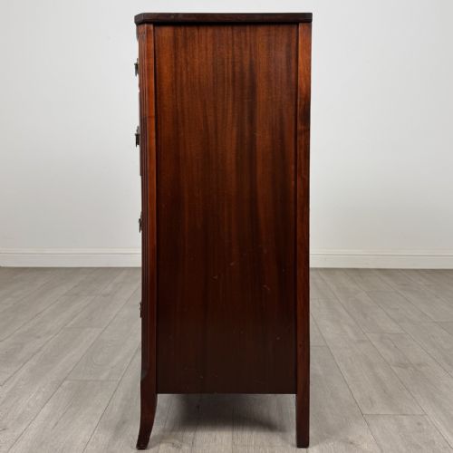 fig 2. An antique mahogany chest of drawers with a bowfront shape, brass oval handles, and reeded side columns.