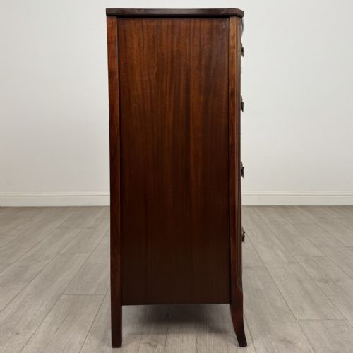 fig 6. An antique mahogany chest of drawers with a bowfront shape, brass oval handles, and reeded side columns.