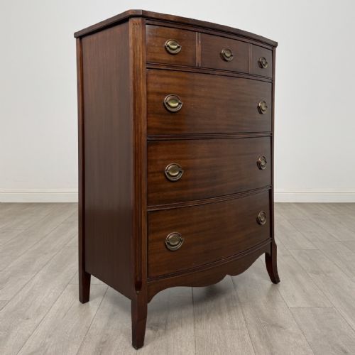 fig 7. An antique mahogany chest of drawers with a bowfront shape, brass oval handles, and reeded side columns.