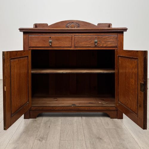 fig 1. An Edwardian dark oak cupboard featuring a raised carved gallery, two top drawers with brass drop handles, and two panelled doors decorated with carved central cartouches.