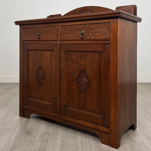 fig 2. An Edwardian dark oak cupboard featuring a raised carved gallery, two top drawers with brass drop handles, and two panelled doors decorated with carved central cartouches.