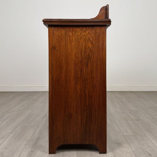 fig 3. An Edwardian dark oak cupboard featuring a raised carved gallery, two top drawers with brass drop handles, and two panelled doors decorated with carved central cartouches.