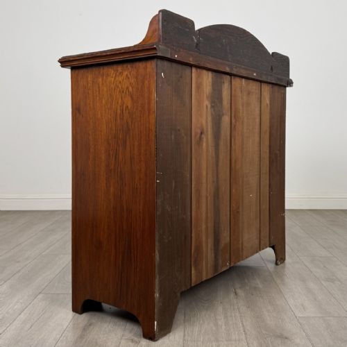 fig 4. An Edwardian dark oak cupboard featuring a raised carved gallery, two top drawers with brass drop handles, and two panelled doors decorated with carved central cartouches.