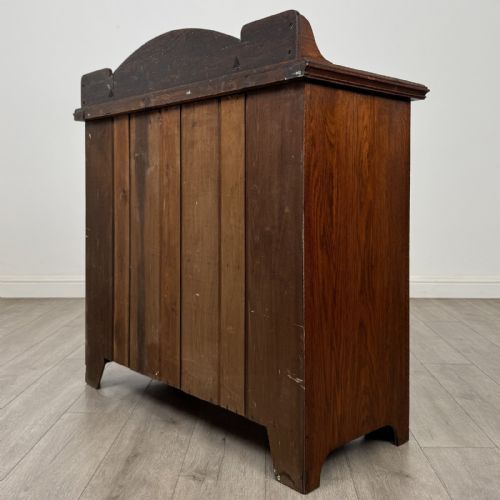 fig 6. An Edwardian dark oak cupboard featuring a raised carved gallery, two top drawers with brass drop handles, and two panelled doors decorated with carved central cartouches.