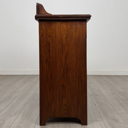 fig 7. An Edwardian dark oak cupboard featuring a raised carved gallery, two top drawers with brass drop handles, and two panelled doors decorated with carved central cartouches.